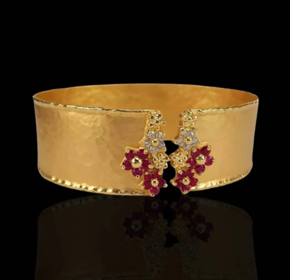 A gold bracelet with red flowers on it.