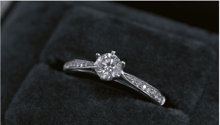 A diamond ring is shown on top of a velvet box.