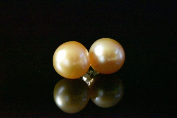 Golden pearl earrings on black background.