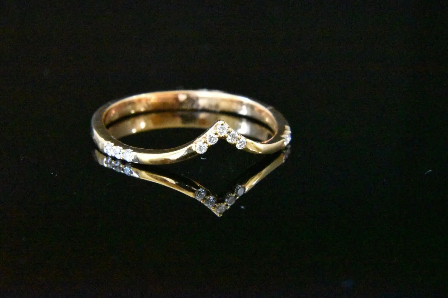 Gold diamond V-shaped ring on black.