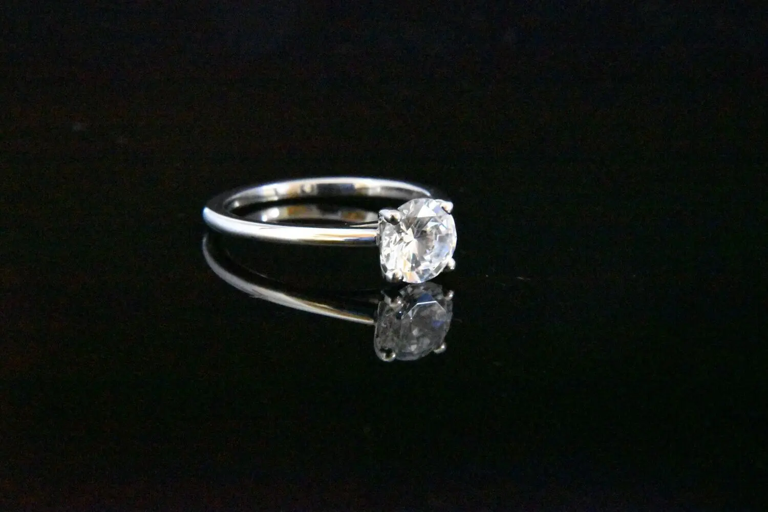 Solitaire diamond ring on black background.