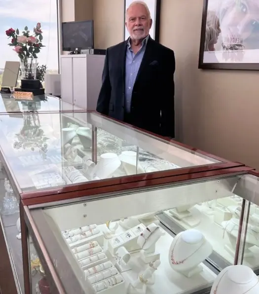 Man in suit stands by jewelry display.